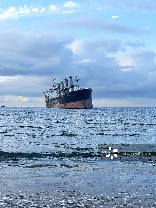 布鲁维斯号货轮在浅海区搁浅，黑棕色船体占据画面主体，天空云层厚重，海面波纹轻抚沙滩图片素材
