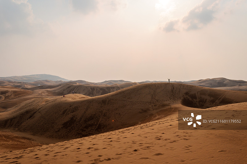 响沙湾的广袤沙漠中一人站立沙丘之巅张开双臂拥抱自然，沙面足迹蜿蜒延伸至远方山脉，光影交错展现沙漠壮美图片素材