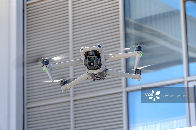 在工业区内巡查的大疆Air3无人机 正在物流仓库区飞行执行安防监控任务的无人机 四旋翼无人飞行器图片素材