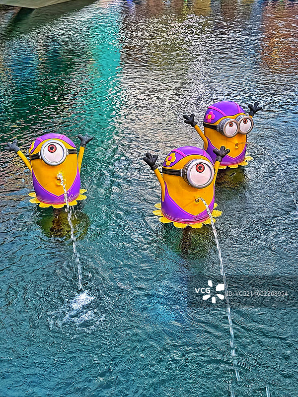 清凉一夏：戏水的小黄人三人组三个戴着泳镜和泳帽、正在喷水的小黄人雕塑图片素材