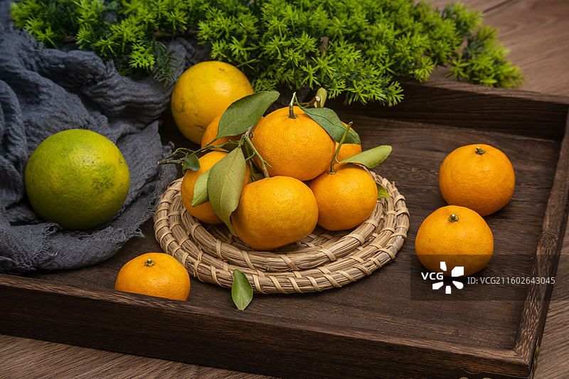 桌面摆放新鲜柑橘砂糖橘与绿叶编织垫静物摆拍图片素材
