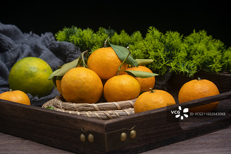 桌面摆放新鲜柑橘砂糖橘与绿叶编织垫静物摆拍图片素材
