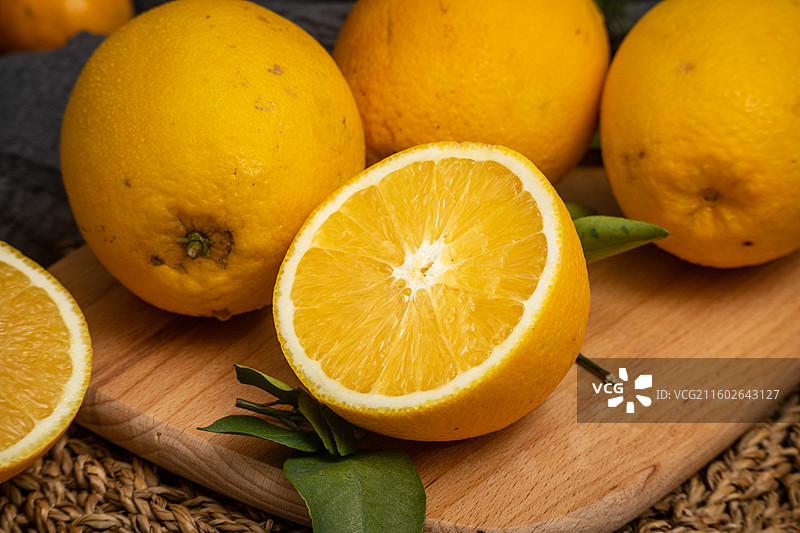 桌面摆放新鲜柑橘橙子脐橙与绿叶编织垫静物摆拍图片素材