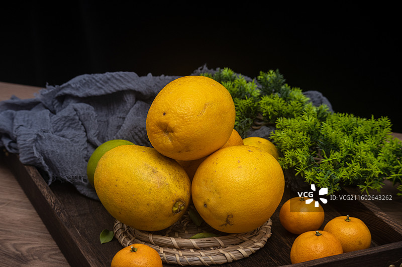 桌面摆放新鲜柑橘橙子脐橙与绿叶编织垫静物摆拍图片素材