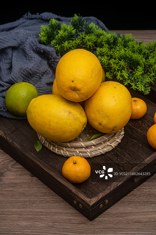 桌面摆放新鲜柑橘橙子脐橙与绿叶编织垫静物摆拍图片素材