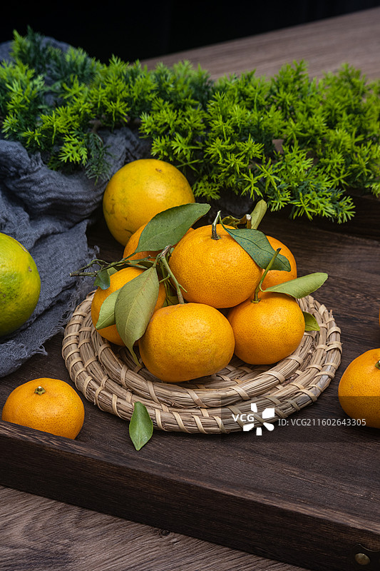 桌面摆放新鲜柑橘砂糖橘与绿叶编织垫静物摆拍图片素材
