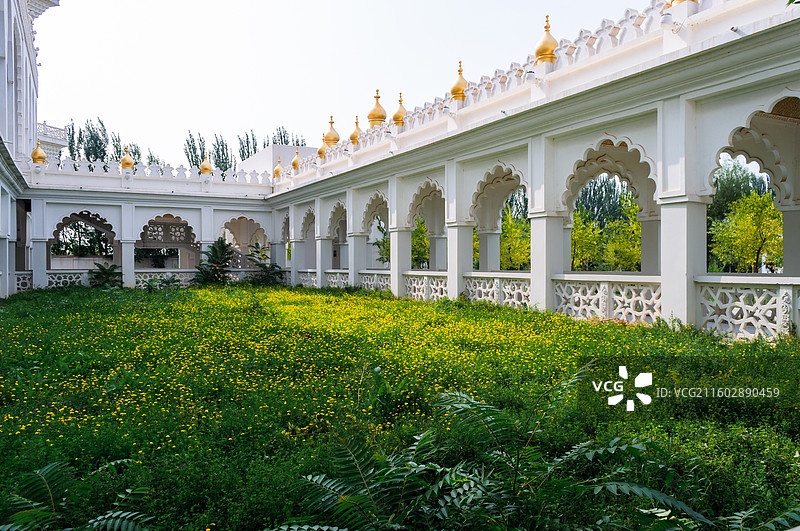 中华回乡文化园中白色拱形长廊环绕金色穹顶与黄色花田，镂空围栏与绿树背景构成静谧景观。图片素材