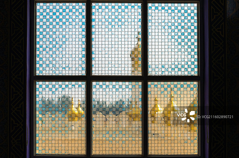 中华回乡文化园中深色窗框六格玻璃窗，蓝白方格图案，窗外可见金色尖顶建筑，光线柔和。图片素材