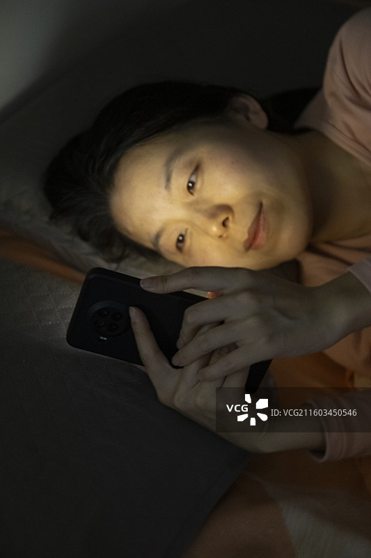 亚洲女士躺床看手机图片素材