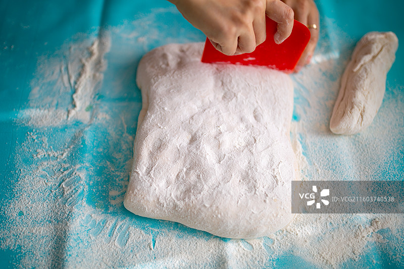 正在用红色刮刀切割撒有面粉的面团图片素材
