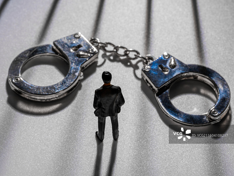 金属手铐、微缩人物与透过铁栏杆的光图片素材