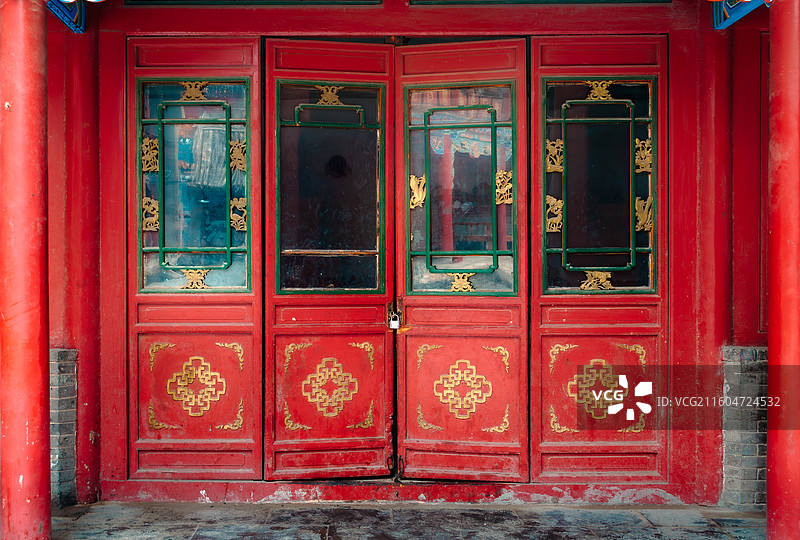 大昭寺中一扇鲜艳大红色中式传统双开门，装饰金色回纹吉祥图案与绿色窗框，中央透明玻璃镶嵌金色雕花图片素材