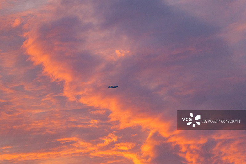 日落时飞机在多云的天空中飞行的低角度视图图片素材