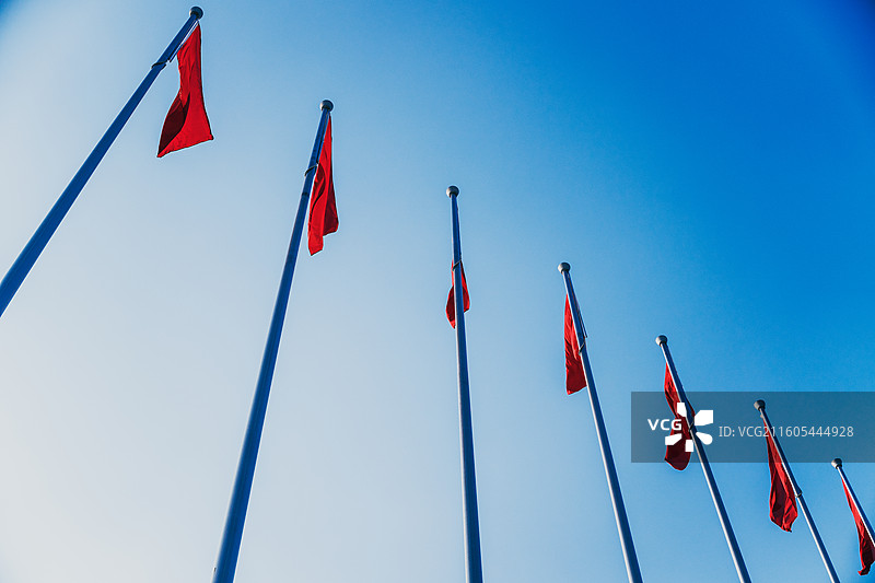 低角度仰拍一排悬挂的鲜艳红旗，在蓝天映衬下迎风飘扬图片素材