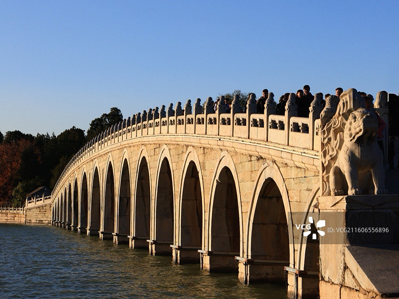 《拱影伴狮》         十七孔桥拱连天际，石狮披暖光。游人缓步，秋林衬古意，把黄昏揉进石纹里。图片素材