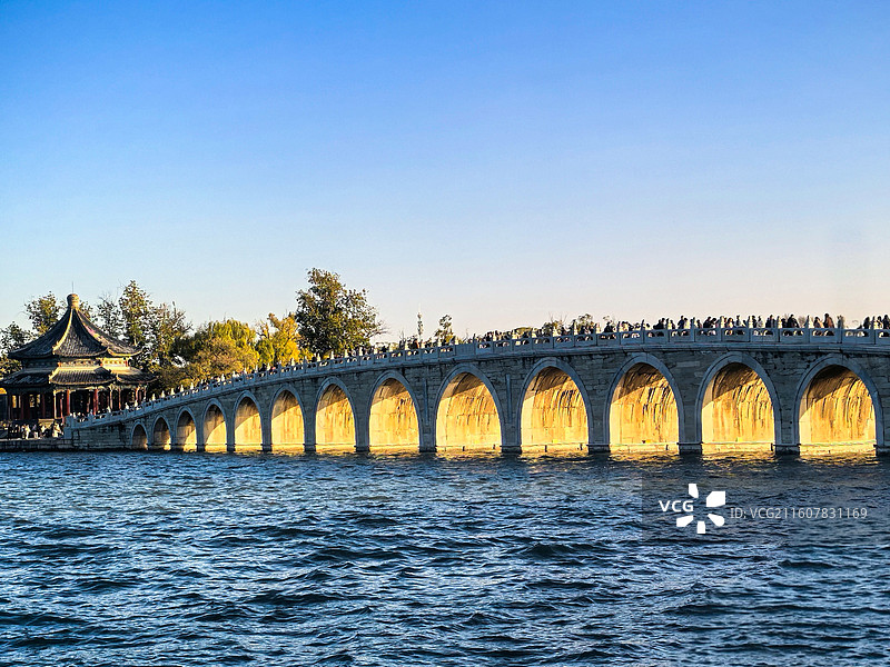 《金洞穿桥》        夕光穿十七孔桥，金辉裹石拱，冷波映蓝天，秋亭伴人潮，颐和园的黄昏正恰好。图片素材