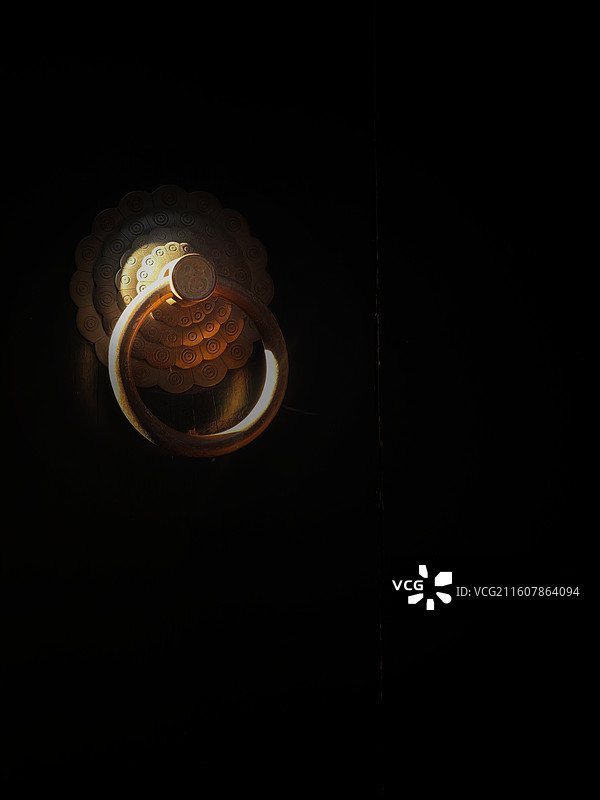 昏暗中，门环圈住了一束光——老铜的纹路裹着暖黄，像把岁月的回响，都锁在了这圈光晕里。图片素材