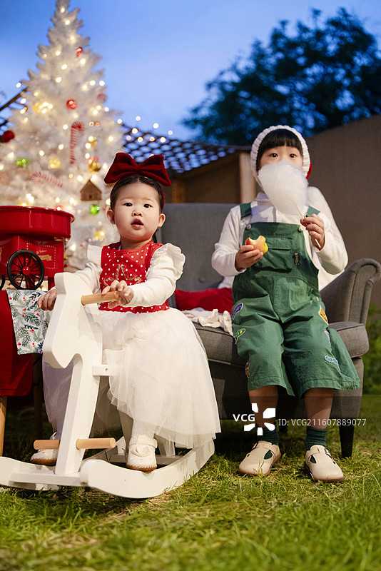 圣诞之夜骑白木马的小女孩与吃棉花糖的小男孩图片素材
