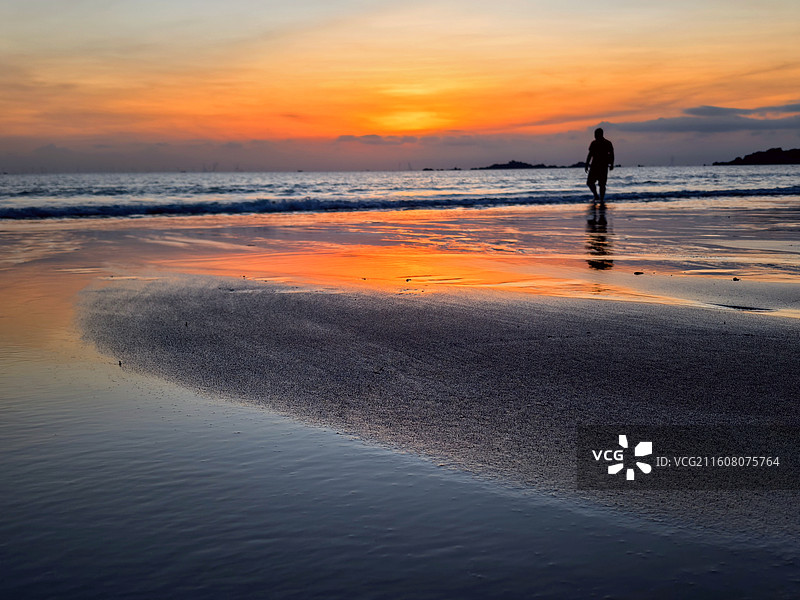 霞染海滩孤影远，天光共潮生 橙黄漫过天海，人影独行潮痕，浪声轻诉黄昏，温柔了岁月的每一寸。图片素材