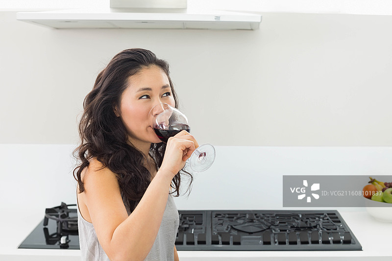 一个盛有红酒的高脚杯，放在白色台面上，旁边是黑色燃气灶，有复制空间图片素材