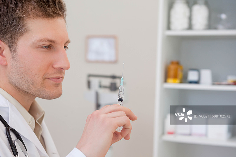 一位穿着白大褂的男医生在诊所里准备注射器，旁边有听诊器和药瓶，留有复制空间图片素材