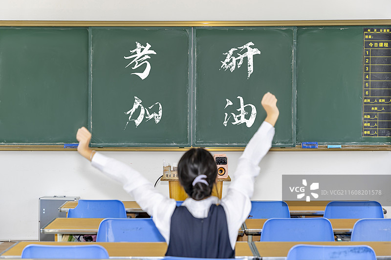 一个女子坐在教室里伸懒腰黑板上写着考研加油图片素材
