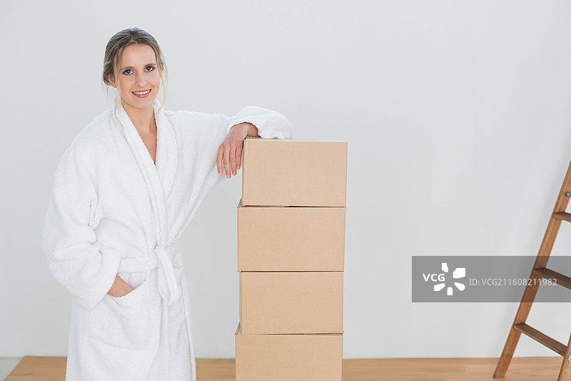 穿着浴袍的成年女性站在房间里，倚靠着梯子旁的箱子堆，有复制空间图片素材