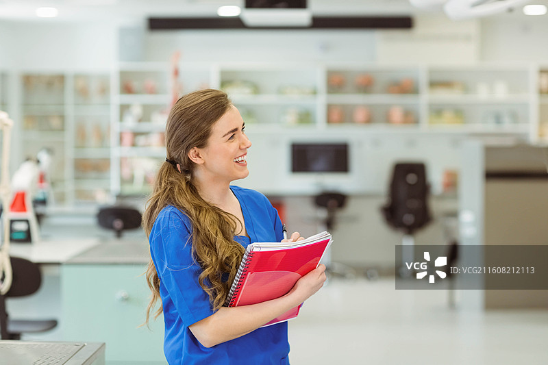 身穿蓝色工作服的女士在临床实验室拿着红色笔记本和粉色文件夹，留有复制空间图片素材