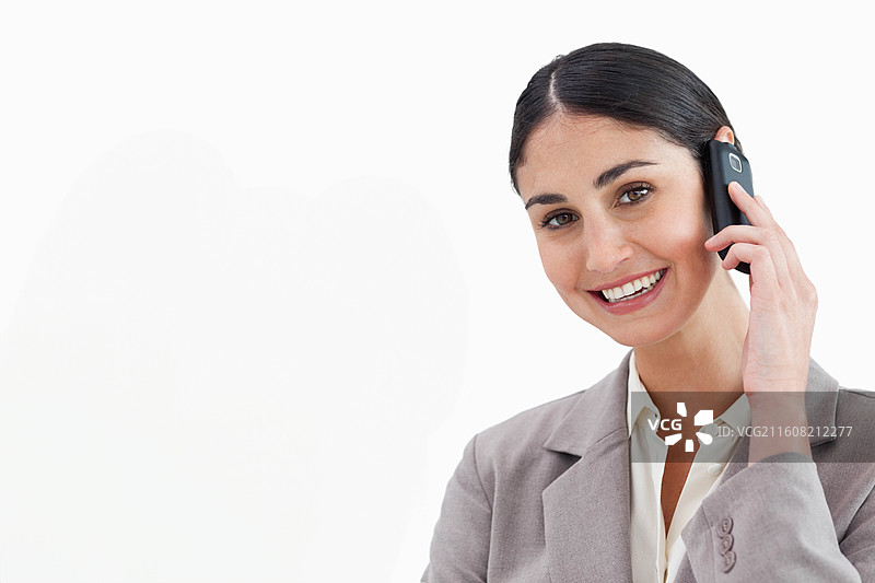 身穿浅灰色西装外套的女子，手持手机，对着白色影棚背景微笑，留有空白空间图片素材