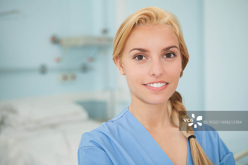 一位穿着蓝色护士服的女护士站在病房的床边，面带微笑面向镜头，留有复制空间图片素材