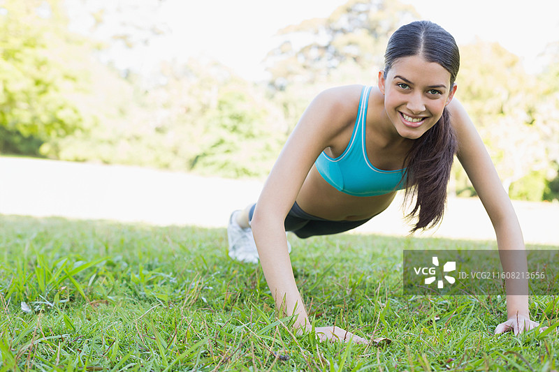穿着蓝绿色运动内衣、黑色短裤和白色鞋子的亚洲女性在草地上做俯卧撑图片素材