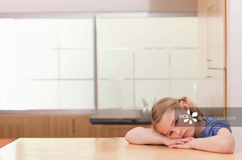 一名学龄女孩在厨房的桌子前，双臂叠放，看着镜头，穿着蓝色上衣，留有复制空间图片素材