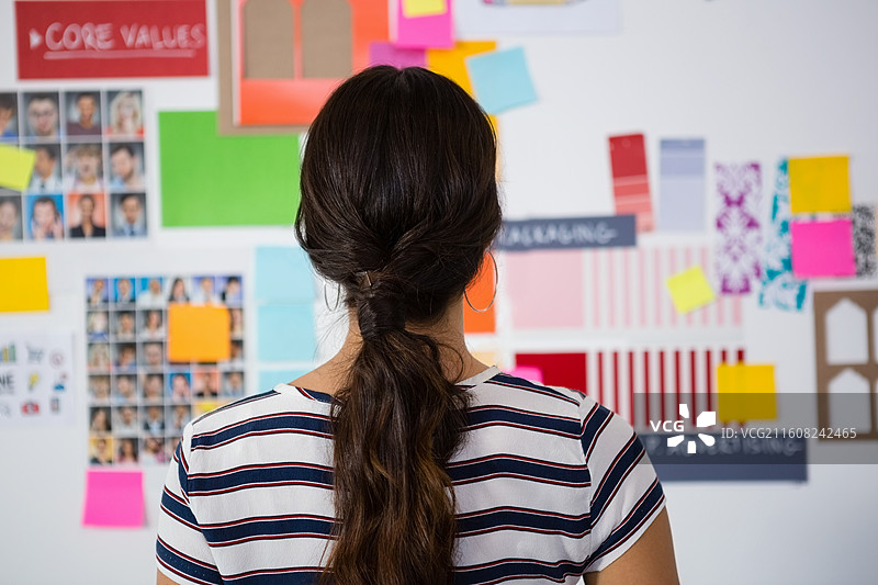 一位穿着T恤的成年女性在工作室里，看着情绪板，同时审阅色卡和肖像画图片素材