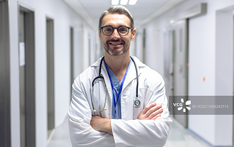 医生双臂交叉，身穿白大褂，佩戴听诊器，站在医院走廊里图片素材