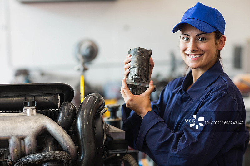 穿着海军蓝工装和帽子、手持启动马达靠近进气歧管的女机械师，留有复制空间图片素材
