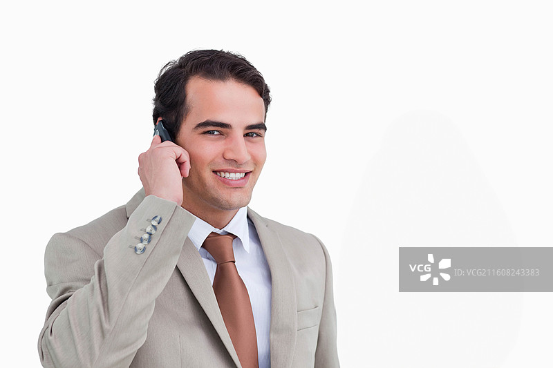 身穿米色西装外套的男士在影棚中一手拿着手机贴近耳朵，脸上带着笑容，摆出造型，留有复制空间图片素材