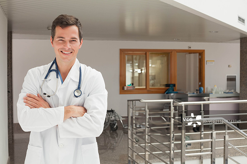 男医生穿着实验服、戴着听诊器，双手抱臂站在接待处，留有复制空间图片素材