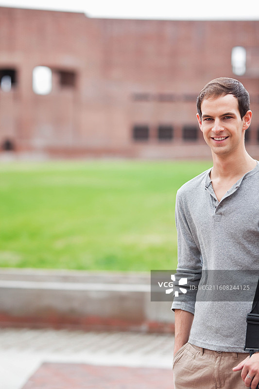 一位20多岁的男子，身穿浅灰色亨利衫，卡其裤，背着背包，站在四边形右侧，有复制空间图片素材