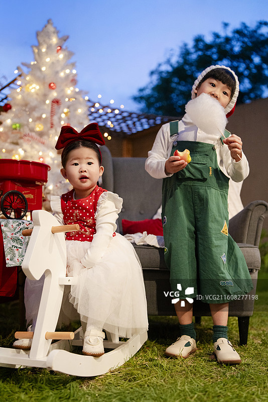 圣诞之夜骑白木马的小女孩与吃棉花糖的小男孩图片素材