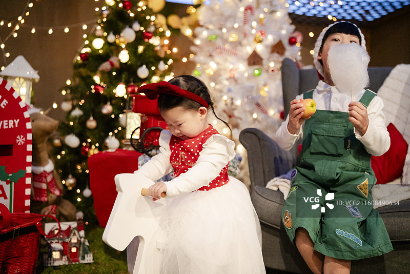 圣诞之夜骑白木马的小女孩与吃棉花糖的小男孩图片素材