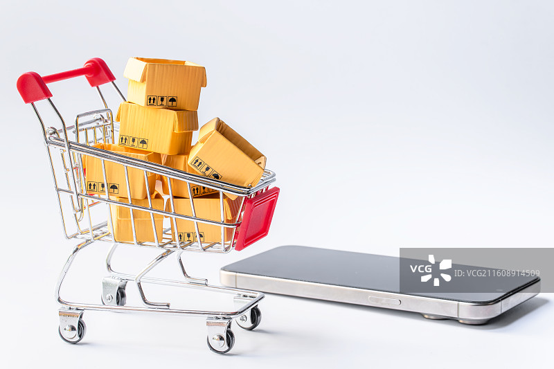 装满货物的购物小推车、手机与白色背景留白图片素材