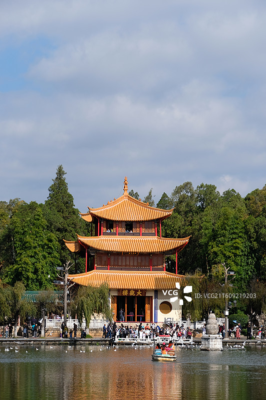 昆明大观楼湖对岸视角摄影 三层飞檐翘角黄琉璃瓦红立柱金色装饰 人群聚集小船停靠 绿树蓝天倒影和谐风光图片素材
