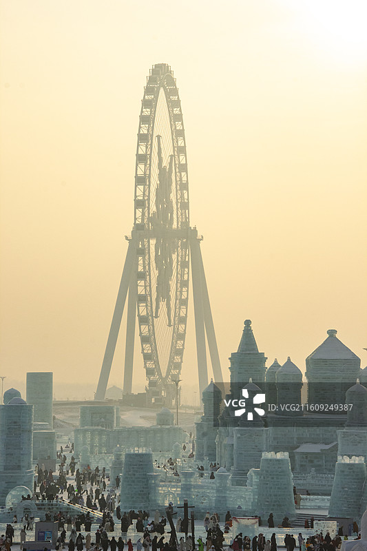 中国黑龙江哈尔滨冰雪大世界游乐场 夕阳余晖暖色调下的冰雕建筑和摩天轮图片素材