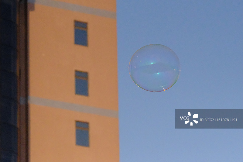 蓝色天空中飘扬的七彩肥皂泡泡。高楼建筑白鸽背景图壁纸图片素材