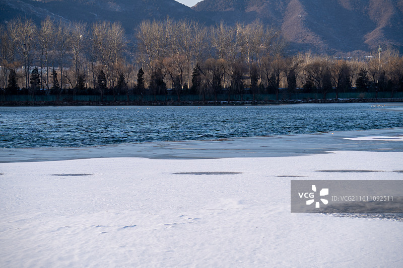 北京颐和园 冬日半结冰湖面雪景与枯树远山自然景观图片素材