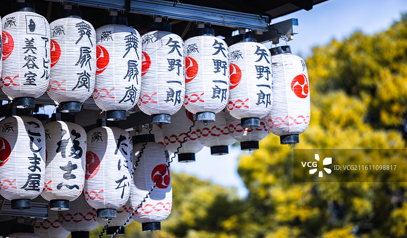 京都寺庙传统白色纸灯笼装饰，红色圆形标记和黑色汉字书法，悬挂于木质屋檐下图片素材