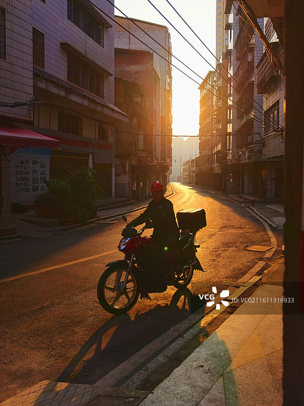 晨阳下的骑行者 晨阳下，骑手戴盔出发，在街巷勾勒出生活逐梦的轨迹。图片素材