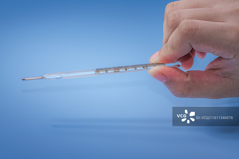蓝色背景下不规则手持水银体温计图片素材