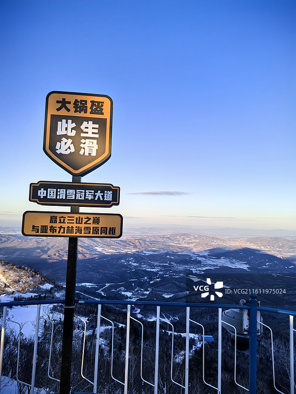 大锅盔滑雪标识牌立在观景台，背后是覆雪的连绵群山，蓝天澄澈。图片素材