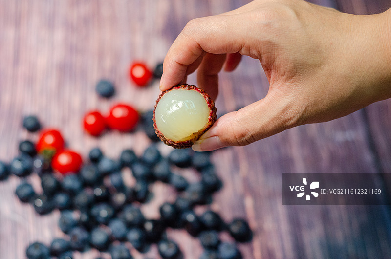 手握剥开的荔枝周围散落蓝莓小番茄图片素材